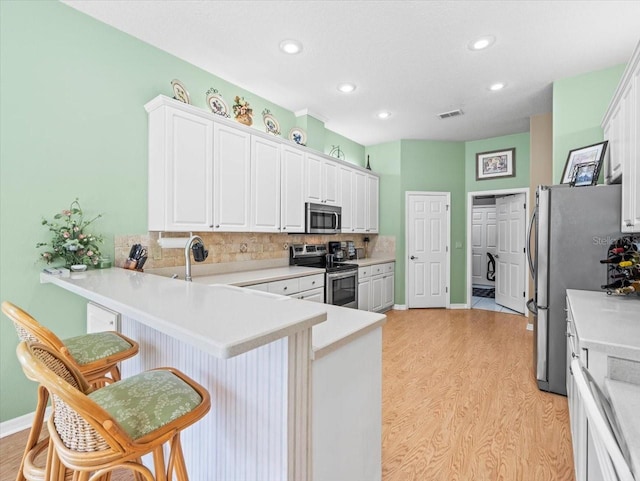 kitchen with light wood-type flooring, white cabinetry, kitchen peninsula, appliances with stainless steel finishes, and a breakfast bar area