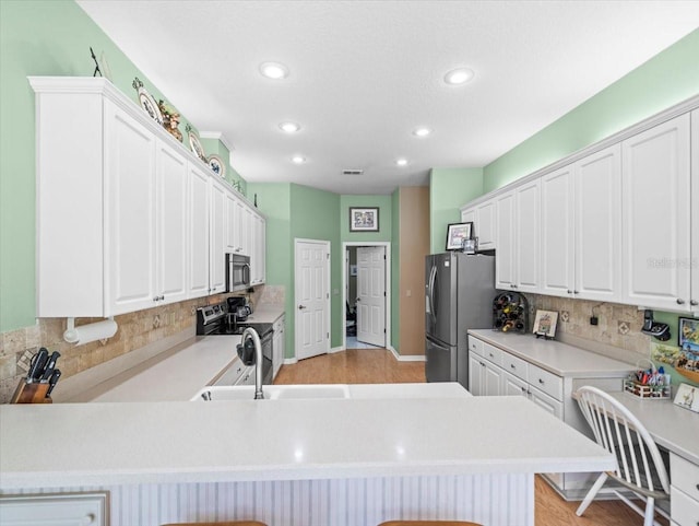 kitchen featuring a breakfast bar, kitchen peninsula, appliances with stainless steel finishes, and white cabinets