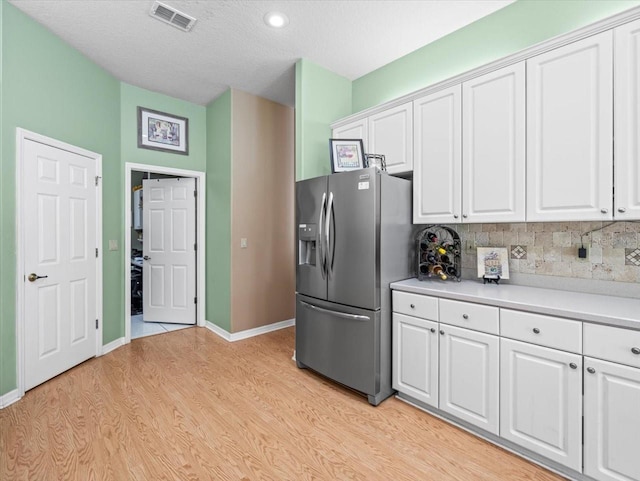 kitchen with a textured ceiling, white cabinetry, light hardwood / wood-style flooring, tasteful backsplash, and stainless steel refrigerator with ice dispenser