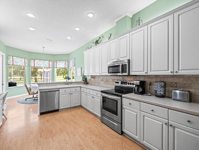 kitchen featuring light wood-type flooring, pendant lighting, stainless steel appliances, and white cabinets