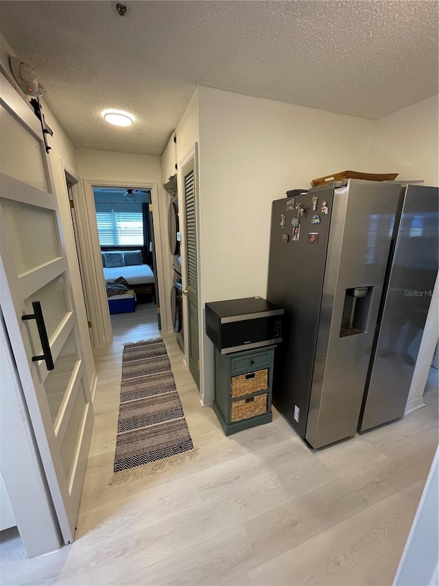 corridor with stacked washer / dryer, a textured ceiling, and light wood-type flooring