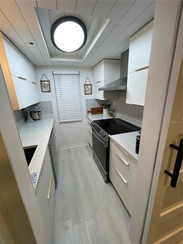 kitchen featuring light hardwood / wood-style floors, white cabinetry, wall chimney range hood, a raised ceiling, and stainless steel electric range