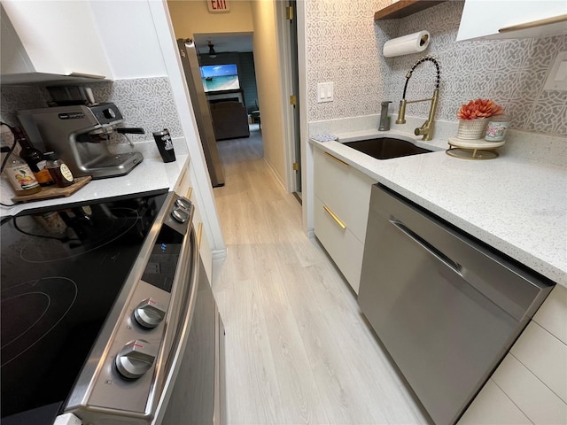 kitchen with light stone countertops, sink, backsplash, appliances with stainless steel finishes, and light wood-type flooring