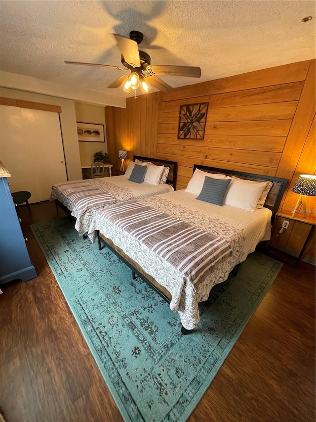 bedroom featuring ceiling fan, a textured ceiling, wood walls, and dark wood-type flooring