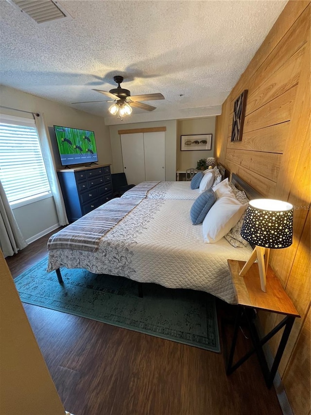 bedroom with wooden walls, ceiling fan, hardwood / wood-style flooring, and a textured ceiling