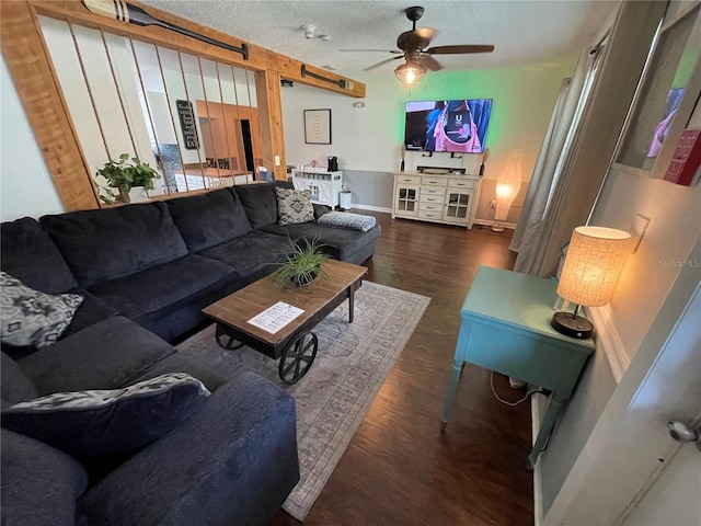 living room with a textured ceiling, dark wood-type flooring, and ceiling fan