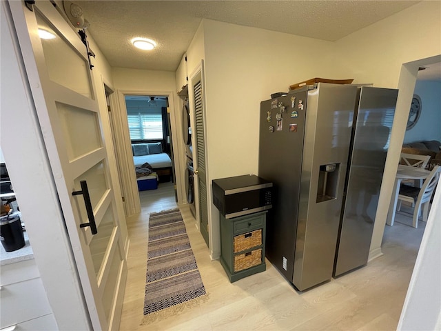 kitchen featuring ceiling fan, stainless steel refrigerator with ice dispenser, light hardwood / wood-style floors, and a textured ceiling