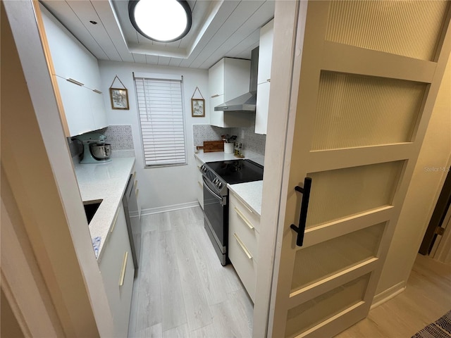 kitchen with white cabinets, black electric range oven, tasteful backsplash, wall chimney range hood, and light hardwood / wood-style floors