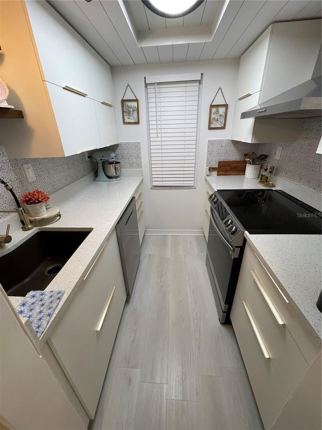 kitchen featuring a tray ceiling, light hardwood / wood-style floors, appliances with stainless steel finishes, and wall chimney range hood