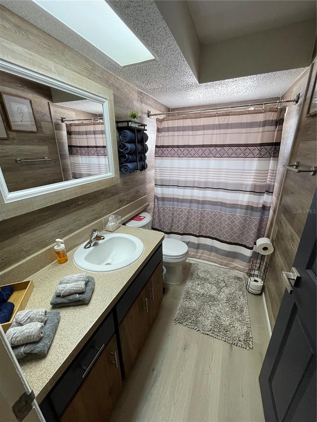 bathroom featuring vanity, a skylight, hardwood / wood-style flooring, toilet, and a shower with shower curtain