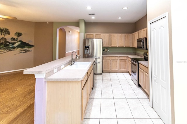 kitchen with appliances with stainless steel finishes, light brown cabinets, light tile patterned floors, a center island with sink, and sink