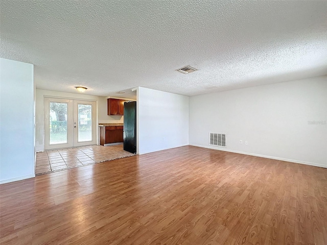 unfurnished living room with a textured ceiling, light hardwood / wood-style floors, and french doors