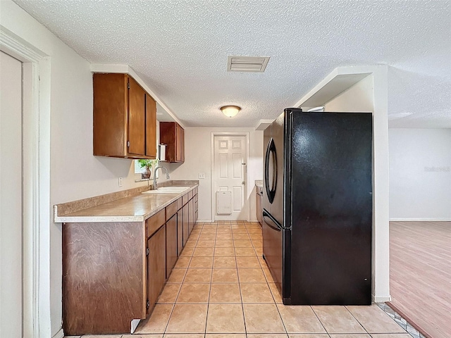 kitchen with light wood-type flooring, a textured ceiling, black fridge, and sink