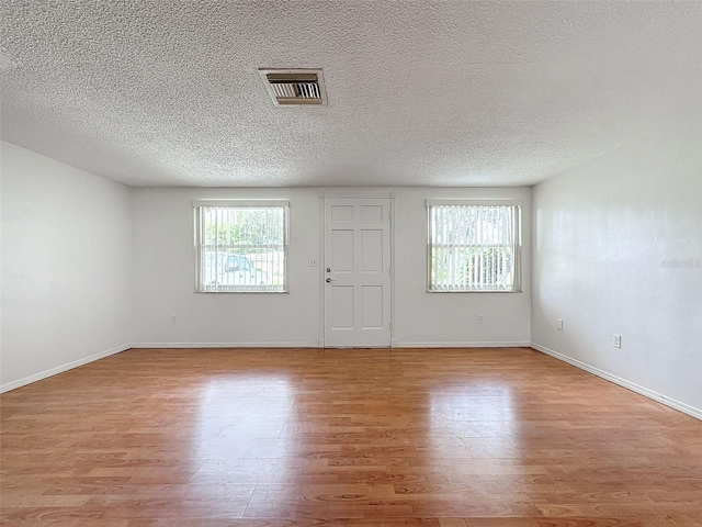 spare room featuring a textured ceiling, light hardwood / wood-style floors, and a wealth of natural light