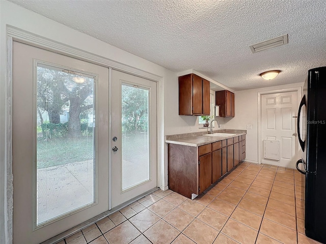 kitchen featuring a textured ceiling, light tile patterned flooring, sink, and black refrigerator