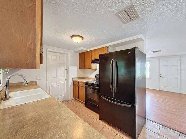 kitchen with a textured ceiling, black appliances, light hardwood / wood-style floors, and sink