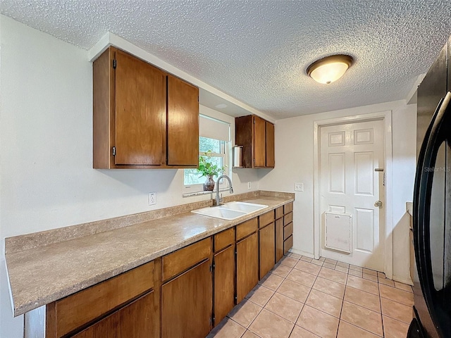 kitchen with a textured ceiling, black fridge, sink, and light tile patterned floors