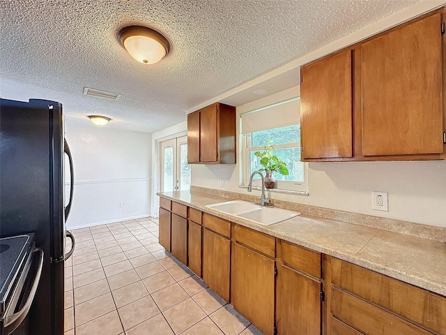 kitchen with a textured ceiling, range with electric stovetop, light tile patterned floors, and sink