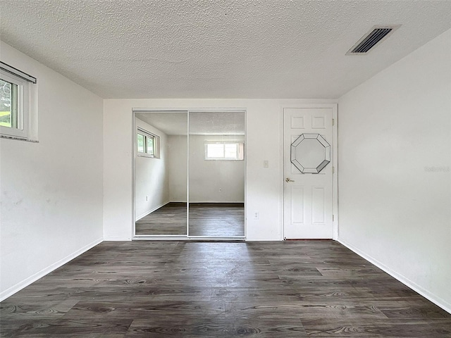 unfurnished bedroom with a textured ceiling, dark hardwood / wood-style floors, and a closet