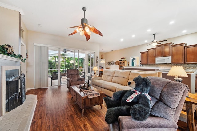 living room featuring a tiled fireplace, ceiling fan, and dark hardwood / wood-style flooring