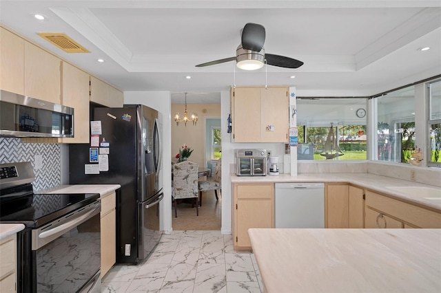 kitchen with ceiling fan with notable chandelier, appliances with stainless steel finishes, a raised ceiling, and light brown cabinets