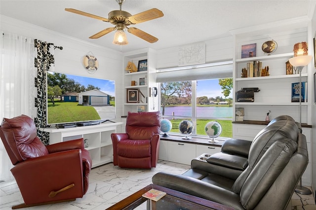 living room featuring ceiling fan, a textured ceiling, ornamental molding, and built in shelves