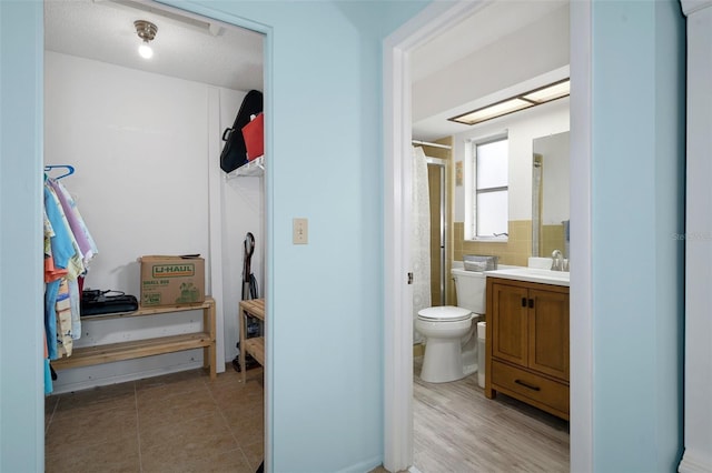 bathroom with tile walls, vanity, a textured ceiling, toilet, and an enclosed shower