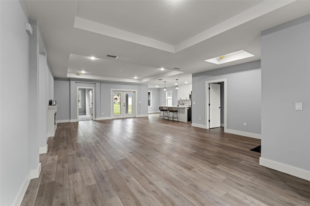 unfurnished living room with french doors, a raised ceiling, and hardwood / wood-style floors