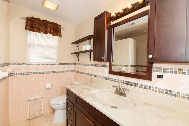 bathroom with tile walls, tile patterned flooring, a textured ceiling, vanity, and toilet