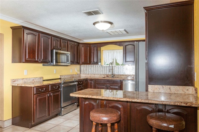 kitchen featuring a breakfast bar, a textured ceiling, tasteful backsplash, appliances with stainless steel finishes, and ornamental molding