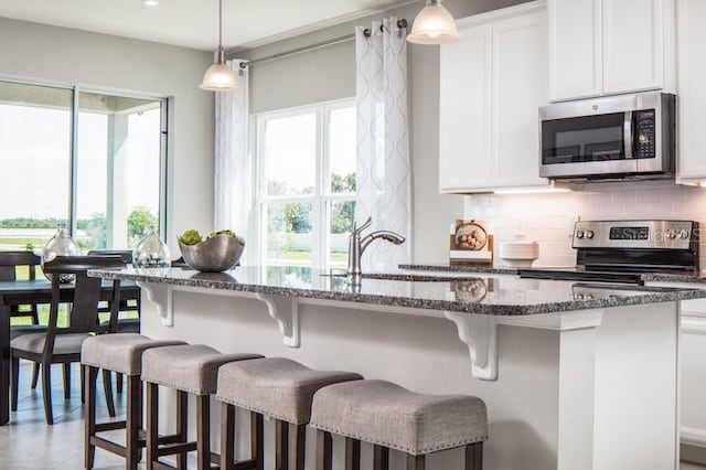 kitchen with a breakfast bar, a wealth of natural light, stainless steel appliances, and decorative light fixtures