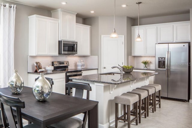 kitchen featuring a kitchen island with sink, a breakfast bar area, sink, appliances with stainless steel finishes, and dark stone countertops