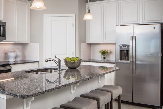 kitchen with dark stone counters, sink, white cabinetry, hanging light fixtures, and stainless steel appliances