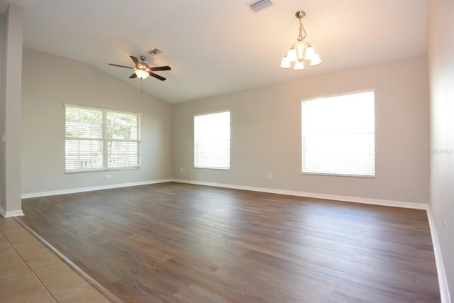 empty room featuring ceiling fan with notable chandelier, vaulted ceiling, and dark wood-type flooring