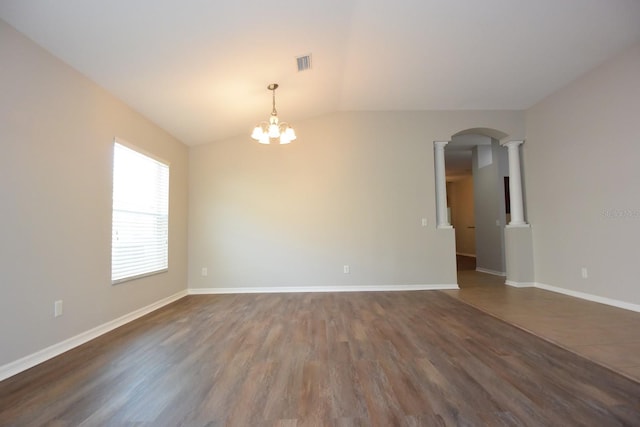 empty room with an inviting chandelier, decorative columns, vaulted ceiling, and dark hardwood / wood-style floors