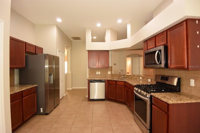 kitchen with sink, light tile patterned floors, high vaulted ceiling, appliances with stainless steel finishes, and light stone countertops