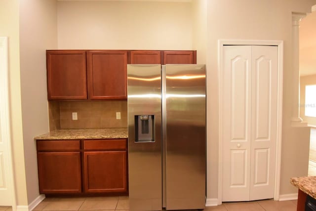 kitchen with light stone counters, stainless steel refrigerator with ice dispenser, decorative columns, and tasteful backsplash