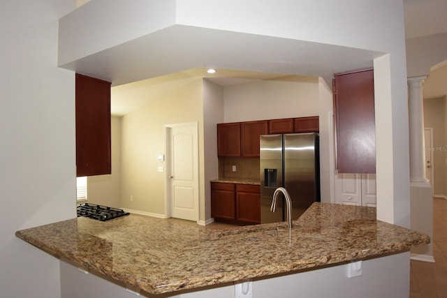 kitchen featuring light stone counters, ornate columns, kitchen peninsula, and stainless steel fridge with ice dispenser