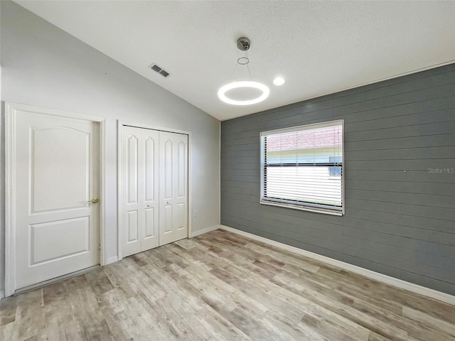 unfurnished bedroom with a closet, light hardwood / wood-style floors, wood walls, and lofted ceiling