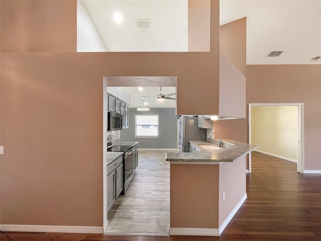 kitchen with kitchen peninsula, stainless steel appliances, light stone counters, high vaulted ceiling, and dark hardwood / wood-style floors