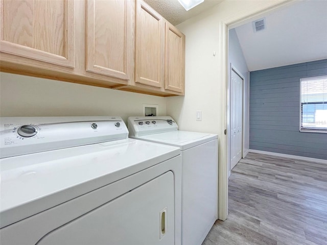 clothes washing area featuring washer and dryer, light wood-type flooring, a textured ceiling, wooden walls, and cabinets