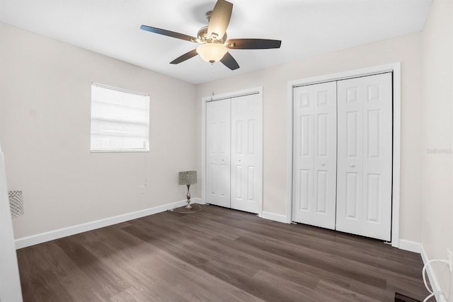 unfurnished bedroom with ceiling fan, two closets, and dark wood-type flooring