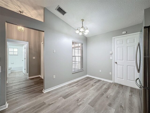 empty room with light wood-type flooring, a textured ceiling, a chandelier, and plenty of natural light