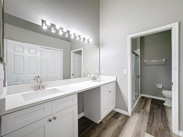 bathroom with hardwood / wood-style floors, a shower with door, toilet, and vanity