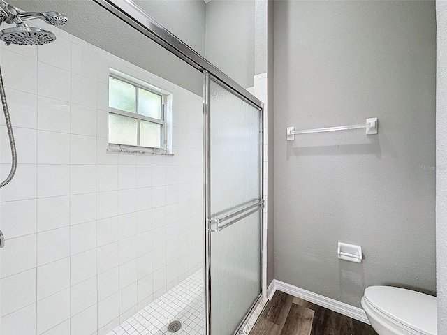 bathroom with wood-type flooring, a shower with shower door, and toilet