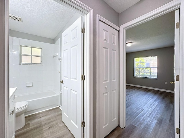 full bathroom with vanity, a textured ceiling, toilet, hardwood / wood-style floors, and tiled shower / bath