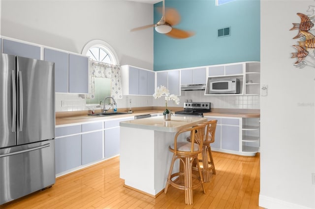 kitchen with a center island, sink, stainless steel appliances, a towering ceiling, and ceiling fan