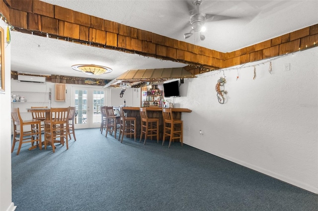 carpeted dining room featuring a textured ceiling, ceiling fan, indoor bar, french doors, and a wall mounted air conditioner