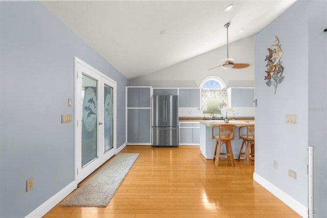 kitchen with light hardwood / wood-style floors, a breakfast bar area, ceiling fan, french doors, and stainless steel fridge