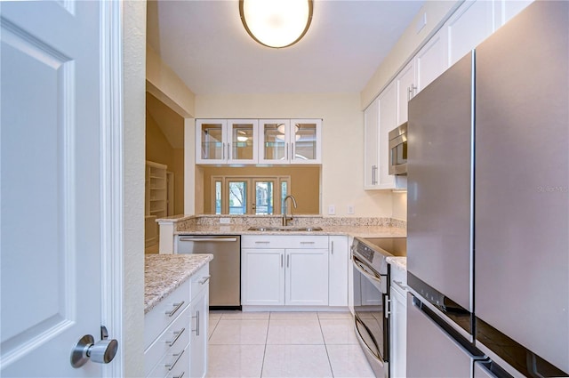 kitchen featuring light tile patterned flooring, sink, light stone counters, stainless steel appliances, and white cabinets